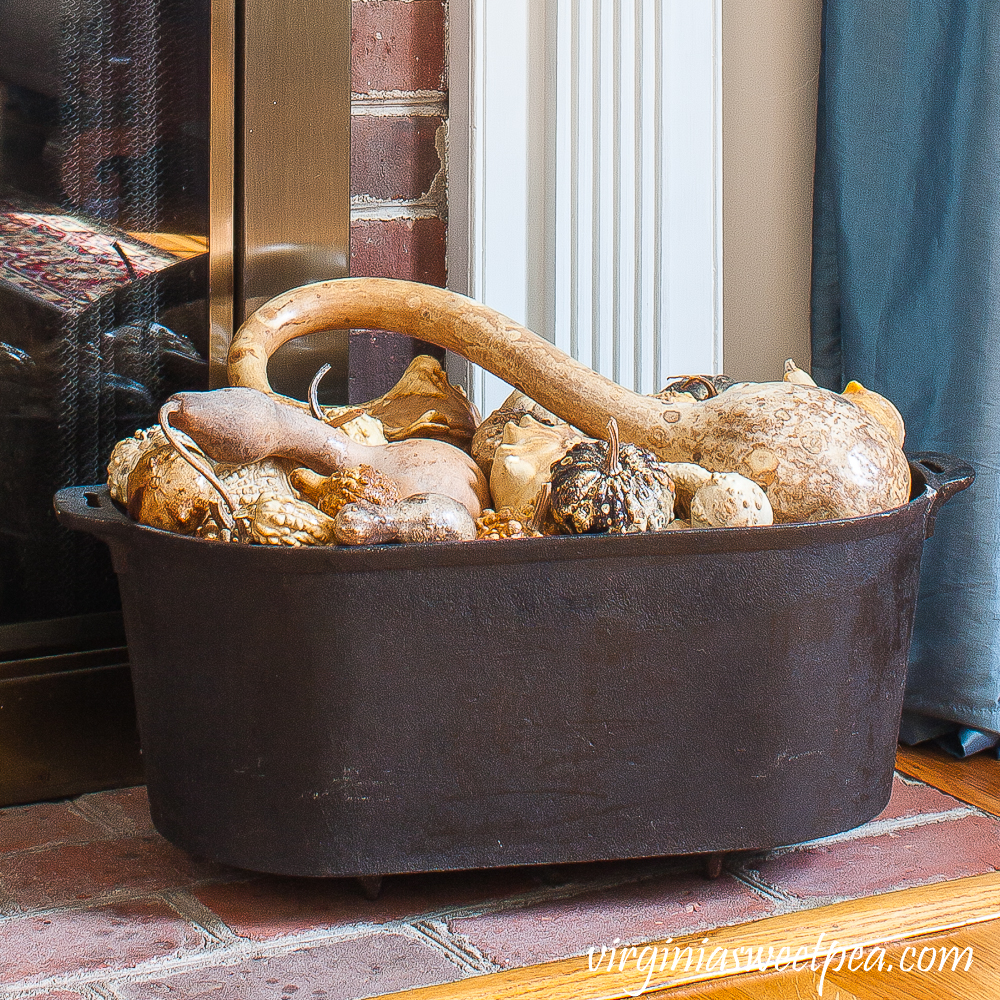 Dried gourds in a black iron tub used on the hearth of a decorated for fall mantel