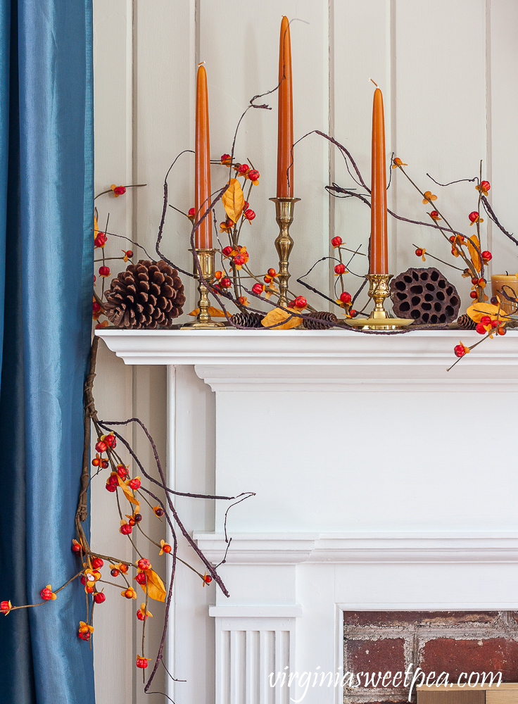 Fall mantel decorated with brass candlesticks with orange candles, bittersweet, lotus pods, and pine cones.