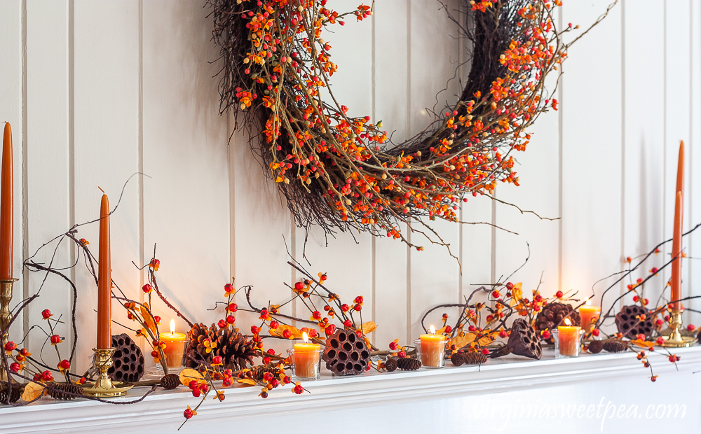 Fall fireplace mantel decorated with bittersweet, lotus pods, pine cones, and candles.