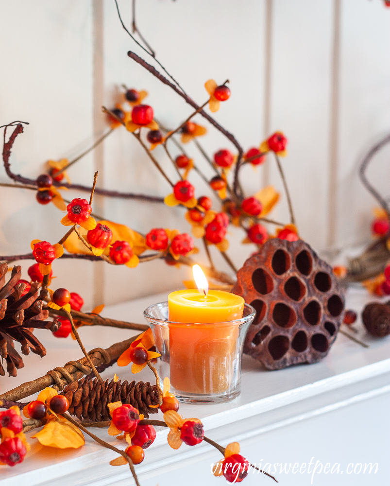 Fall mantel decor with candles, bittersweet, lotus, and pine cones.