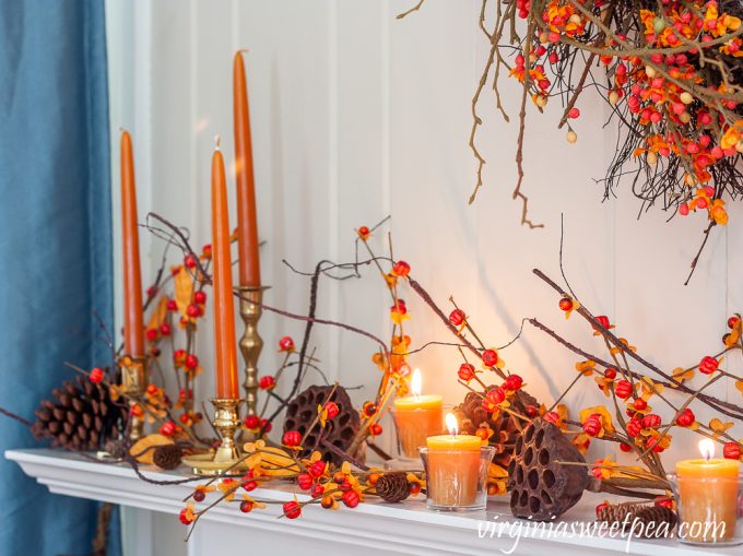 Fall mantel decor with brass candlestick holders, candles, bittersweet, lotus, and pine cones.