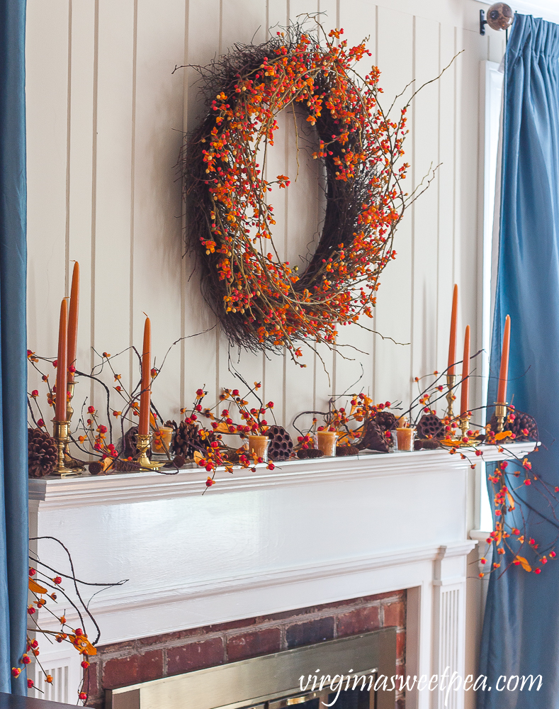 Mantel decorated for fall with bittersweet, lotus pods, pine cones, and candles.