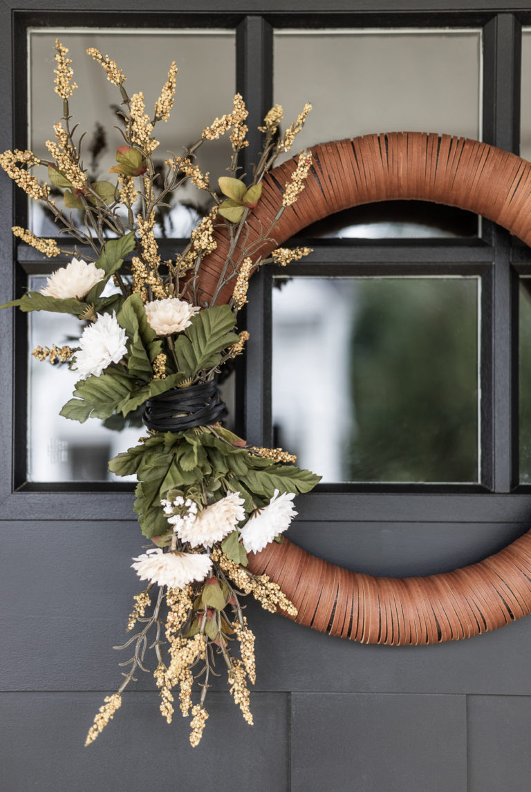 Wreath form wrapped in leather strips decorated for fall with faux florals