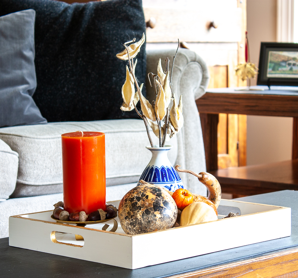 Wood tray painted white and gold styled for fall with dried gourds, acorns, mini pumpkins, an orange candle accented with acorns, and a blue chinoiserie vase