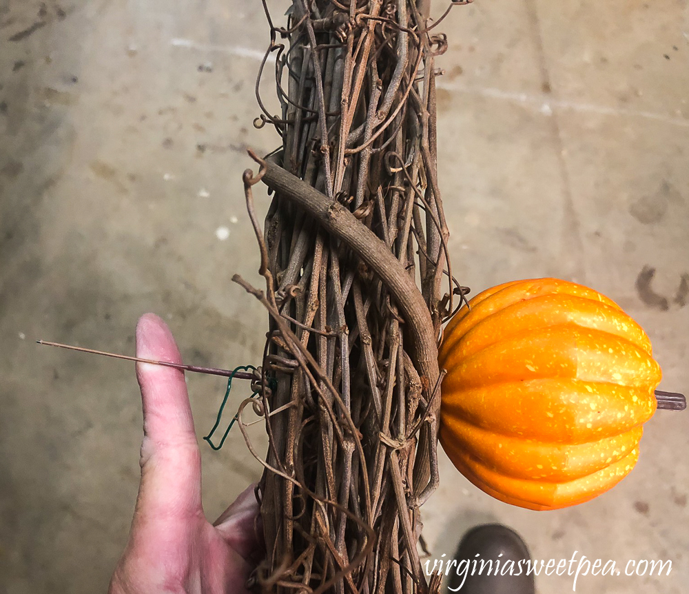 Putting a pumpkin pick on a grapevine wreath.