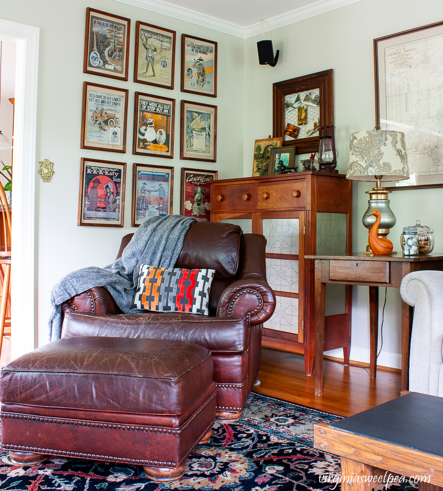Corner of a family room with a leather chair and ottoman, pie safe, framed early 1900s sheet music.