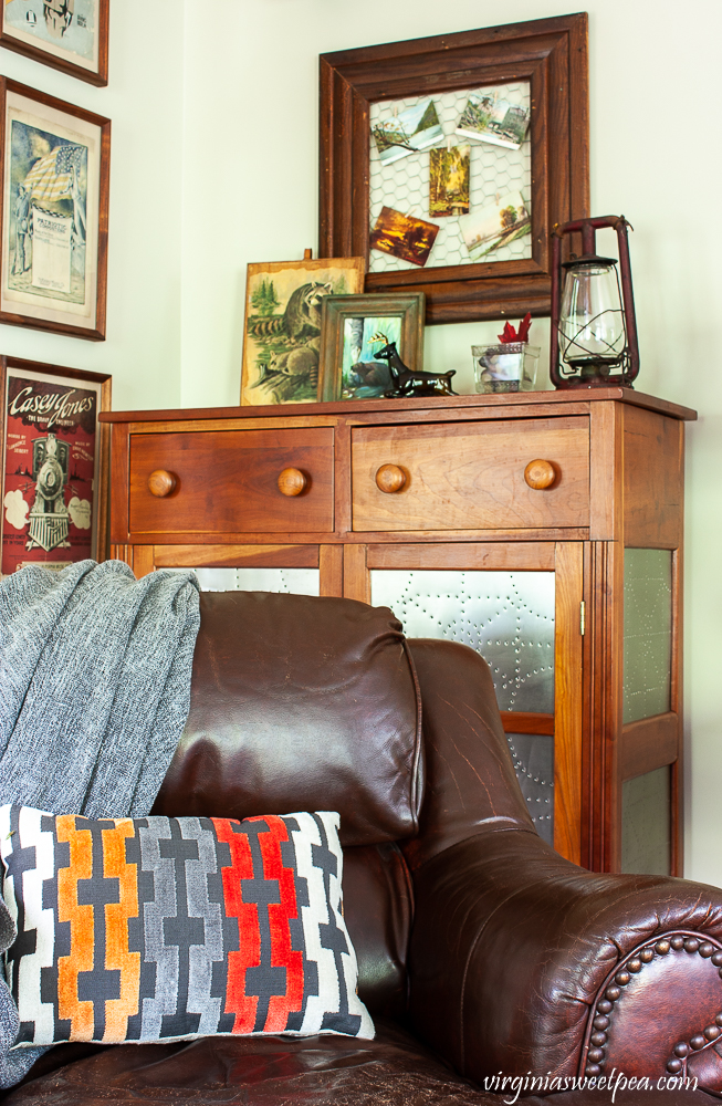 Corner of a family room with a leather chair, pie safe decorated with rustic fall items.