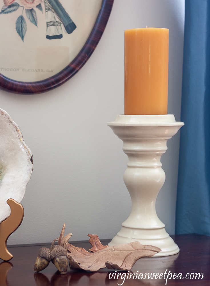 Burnt yellow candle on a creamy white ceramic candle holder with a pottery leaf and pottery acorns.