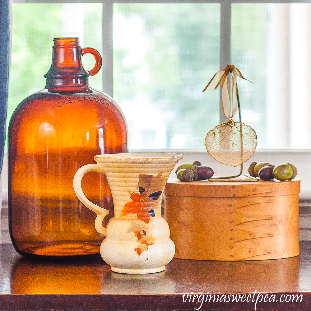 Fall Vignette with amber jug, vintage pitcher with leaves on it, wood box topped with a gold dipped leaf and acorns.