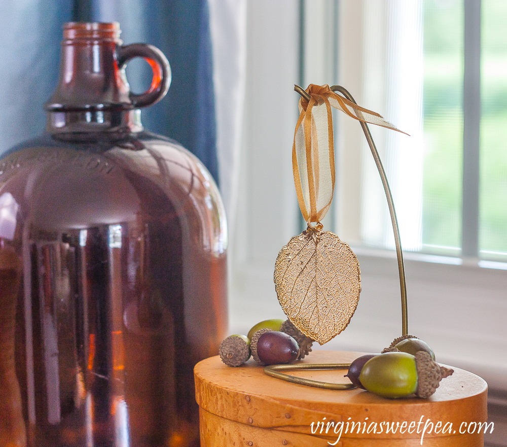 Gold leaf on a hanger with acorns displayed on a wood box with an amber jug