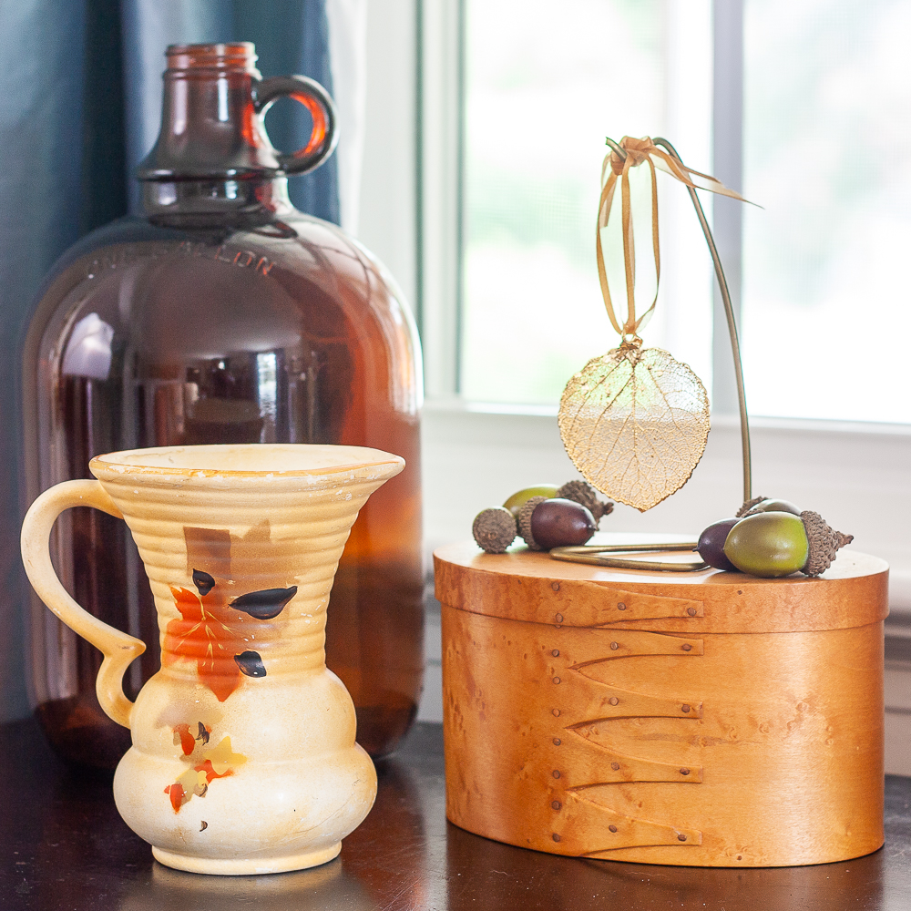 Fall Vignette with amber jug, vintage pitcher with leaves on it, wood box topped with a gold dipped leaf and acorns.