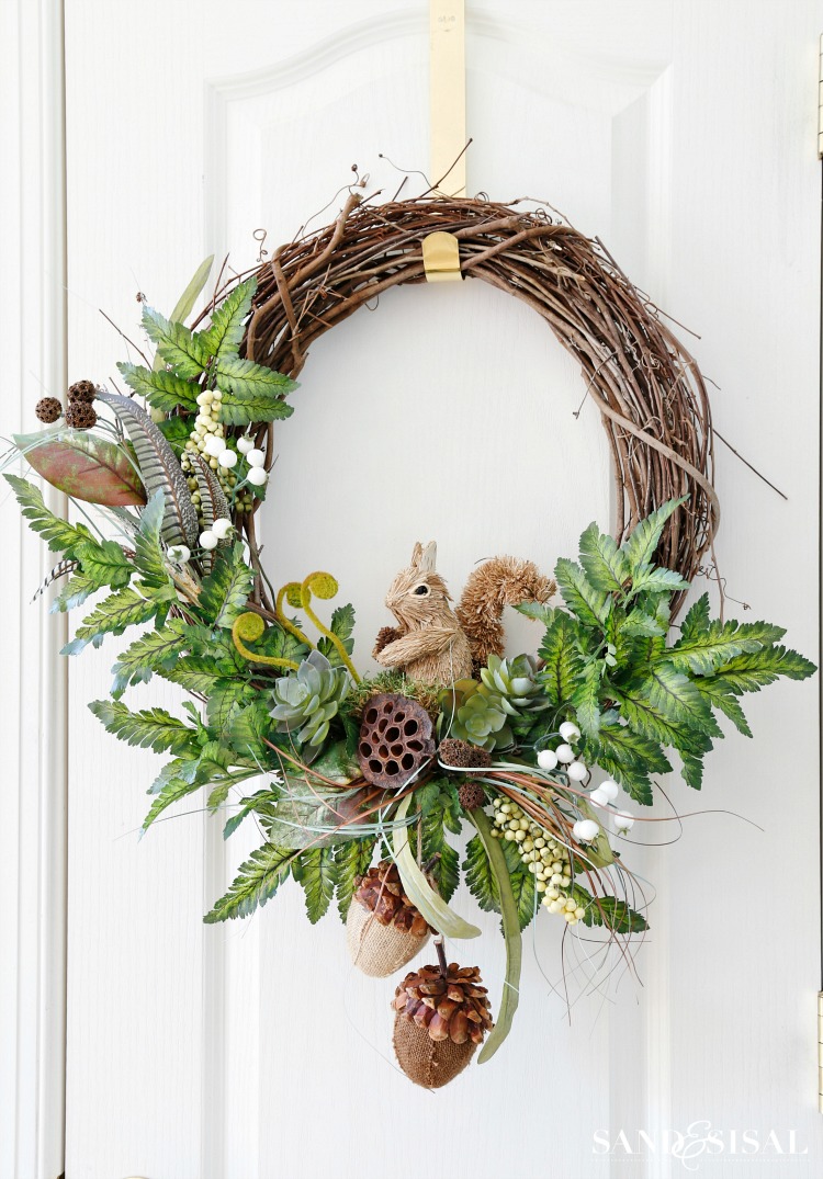 Fall wreath decorated in a woodland style with a squirrel, green foliage, large acorns, and feathers