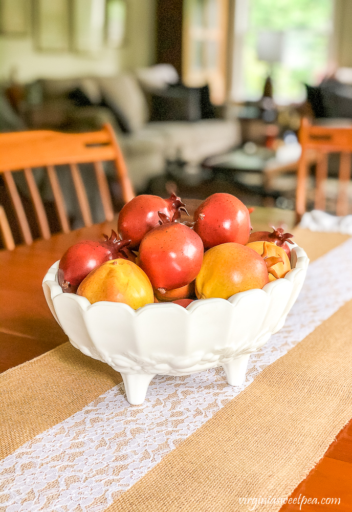 Faux pomegranates in a vintage milk glass footed compote on a dining room table with a burlap table runner accented with lace.aux pomegranates in a vintage milk glass footed compote