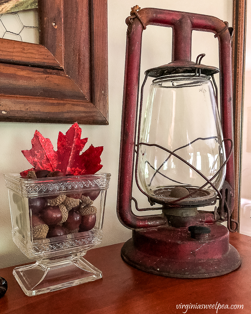Vintage glass footed compote filled with faux acorns and a red leaf and a vintage red lantern
