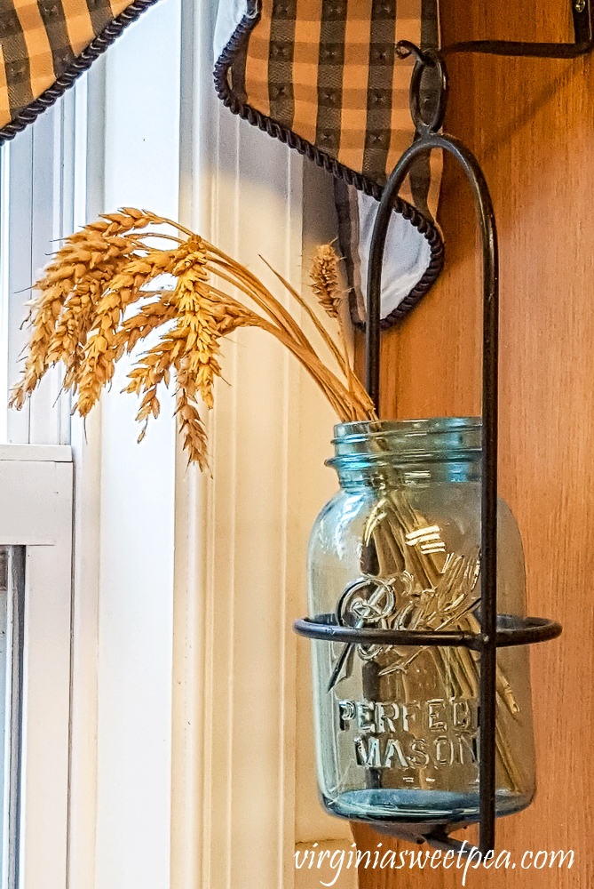 Ball Perfect Mason jar filled with wheat hanging on the side of a cabinet.