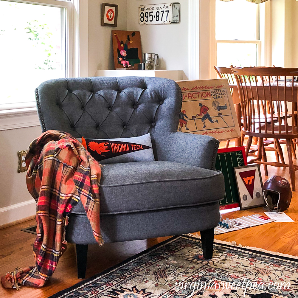 Corner reading nook with gray chair, plaid throw, Virginia Tech pillow, and vintage football collectibles.