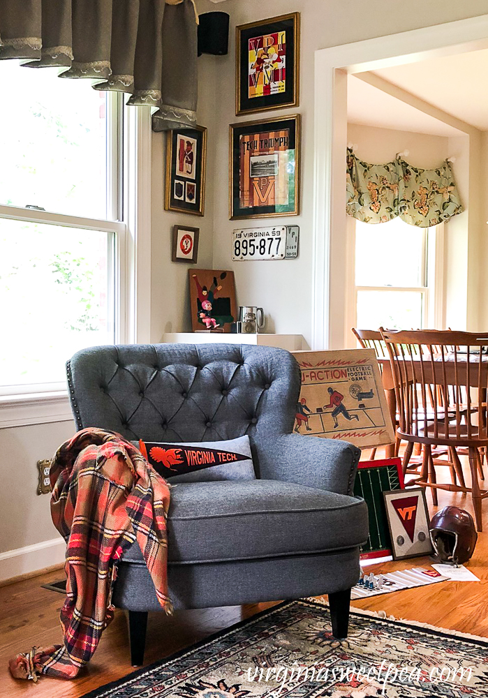 Corner reading nook with gray chair, plaid throw, Virginia Tech pillow, and vintage football collectibles.