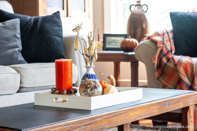 Fall coffee table vignette with a wood tray painted white with gold accents decorated with dried gourds, acorns, mini pumpkins, an orange candle accented with acorns, and a blue chinoiserie vase