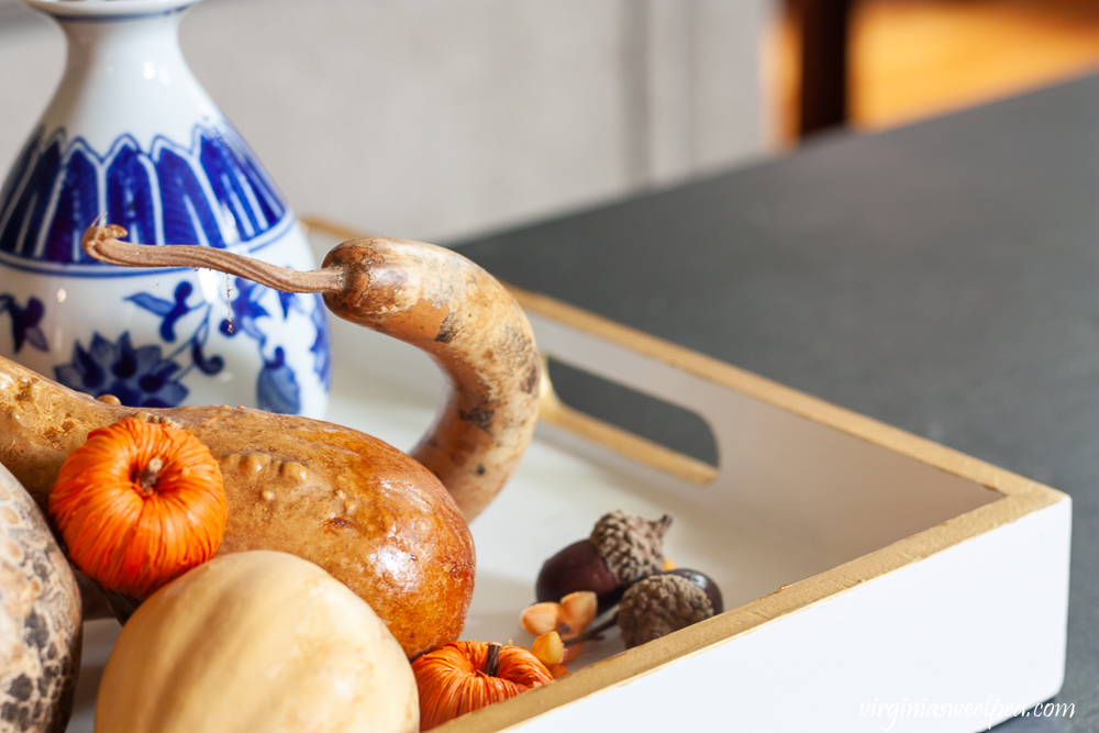 Dried gourds, pumpkins, acorns, and a blue and white chinoiserie vase used to style a tray for fall.