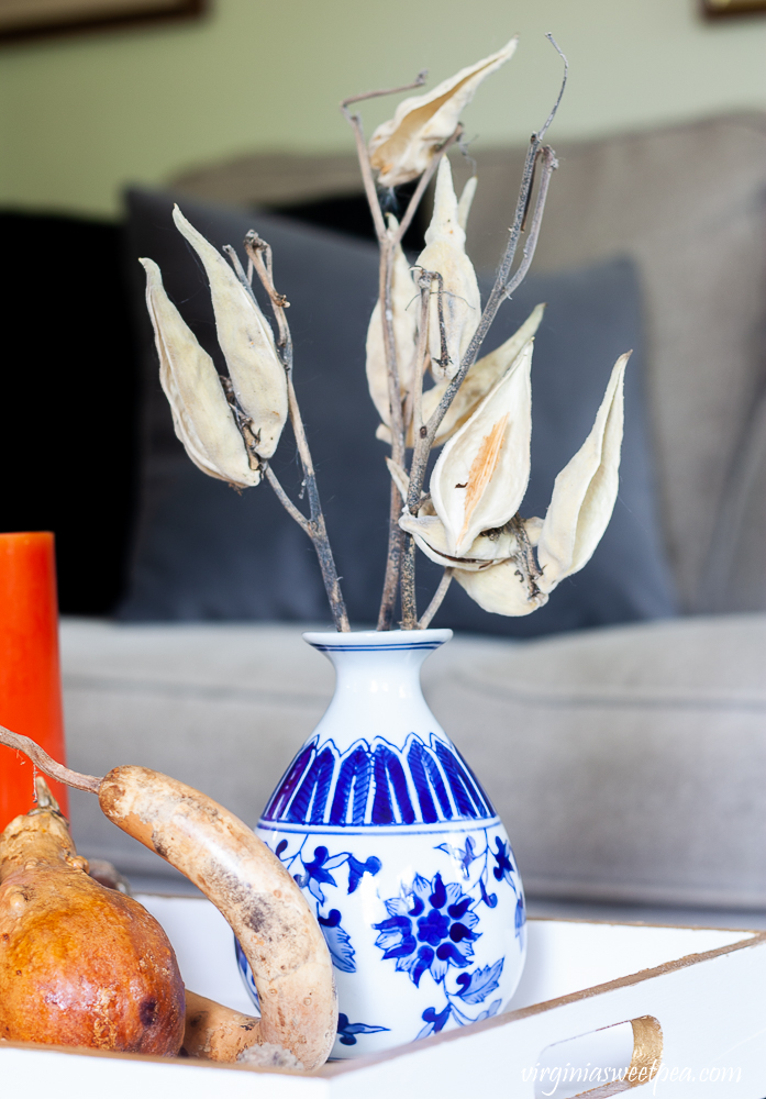 Chinoiserie blue and white vase filled with seed pods on a tray painted white with gold accents.