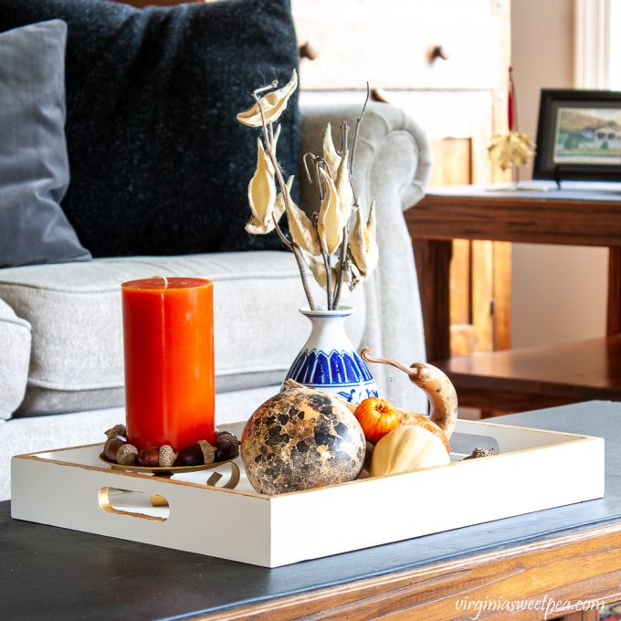 Wood tray painted white and gold styled for fall with dried gourds, acorns, mini pumpkins, an orange candle accented with acorns, and a blue chinoiserie vase