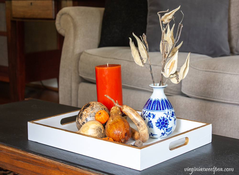 Wood tray painted white and gold styled for fall with dried gourds, acorns, mini pumpkins, an orange candle accented with acorns, and a blue chinoiserie vase