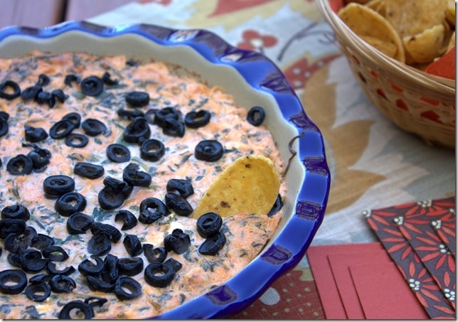 Baked dip made with spinach, salsa, cream cheese, Monterey Jack cheese, and sprinkled with black olvies.