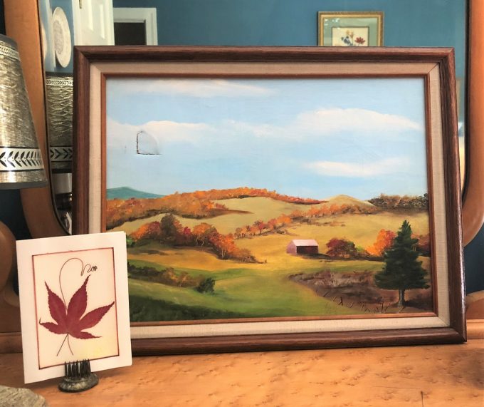 Painting of rolling hills in Vermont in fall and pressed maple leaf