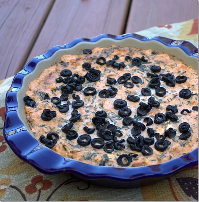 Baked dip made with spinach, salsa, cream cheese, Monterey Jack cheese, and sprinkled with black olvies.