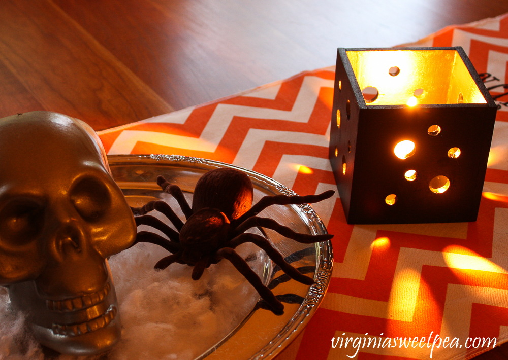 Skull and spider on a silver tray with a orange and white chevron table runner and black square candle holder