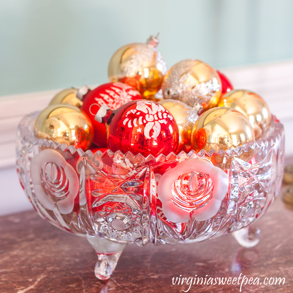 Antique glass bowl filled with vintage red and gold Christmas ornaments