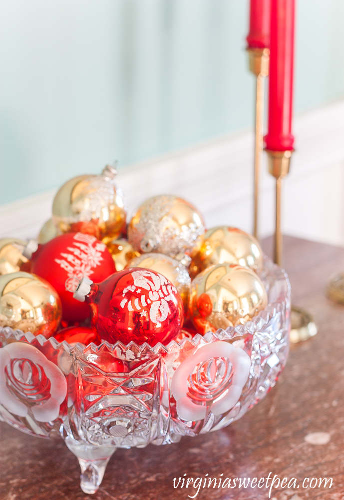 Glass bowl filled with vintage red and gold Christmas ornaments in a dining room decorated for Christmas