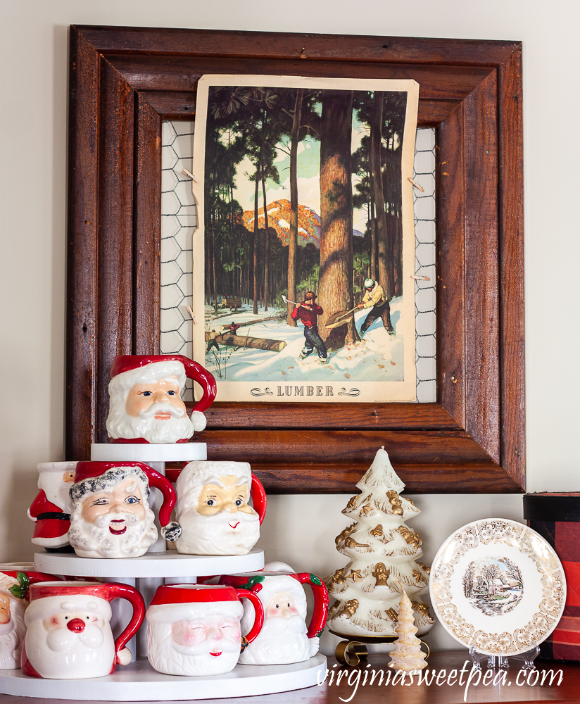 Vintage Santa mugs with vintage Christmas candles, a Knowles plate, vintage Coke lumber poster, and tartan sewing basket
