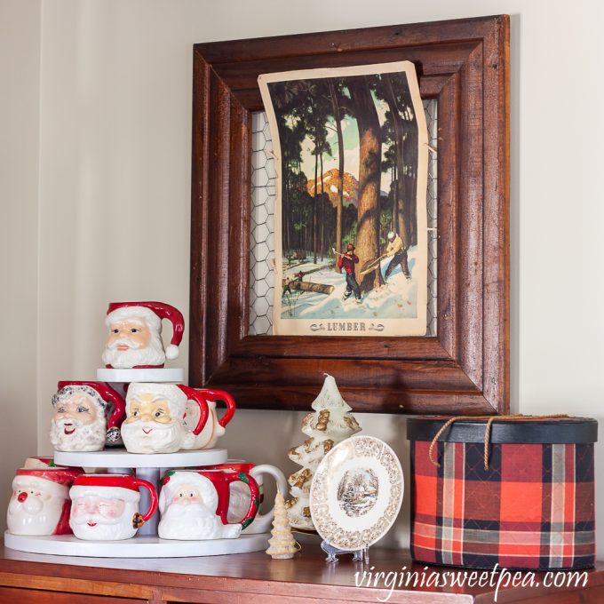 Vintage Santa mugs with vintage Christmas candles, a Knowles plate, vintage Coke lumber poster, and tartan sewing basket