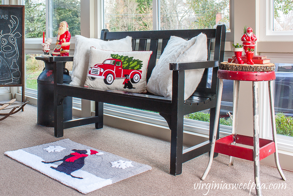 Porch decorated with a bench with a red truck and black lab and a black lab Christmas rug