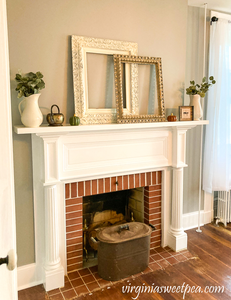 1857 farmhouse mantel styled with two antique frames, white pitchers with Eucalyptus, copper kettle and a coper pot.