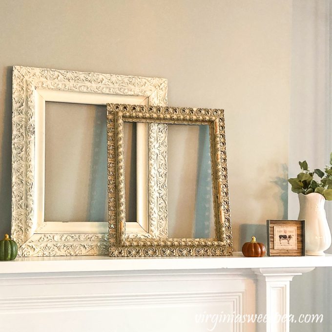 Two antique frames, one white, one gold, with a pumpkin, cow picture, and white pitcher filled with Eucalyptus