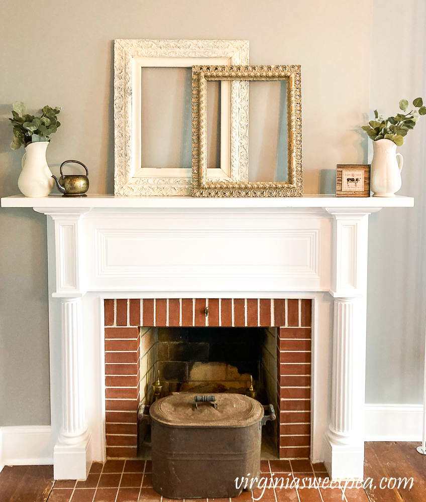 Mantel in an 1857 farmhouse styled with antique frames, white pitchers, brass kettle, copper pot