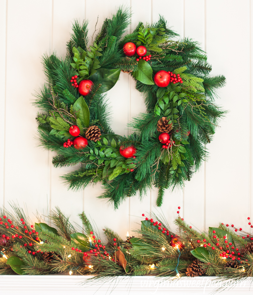 Christmas mantel with Williamsburg wreath and lighted garland on the mantel with red berries, Magnolia, and pine cones.