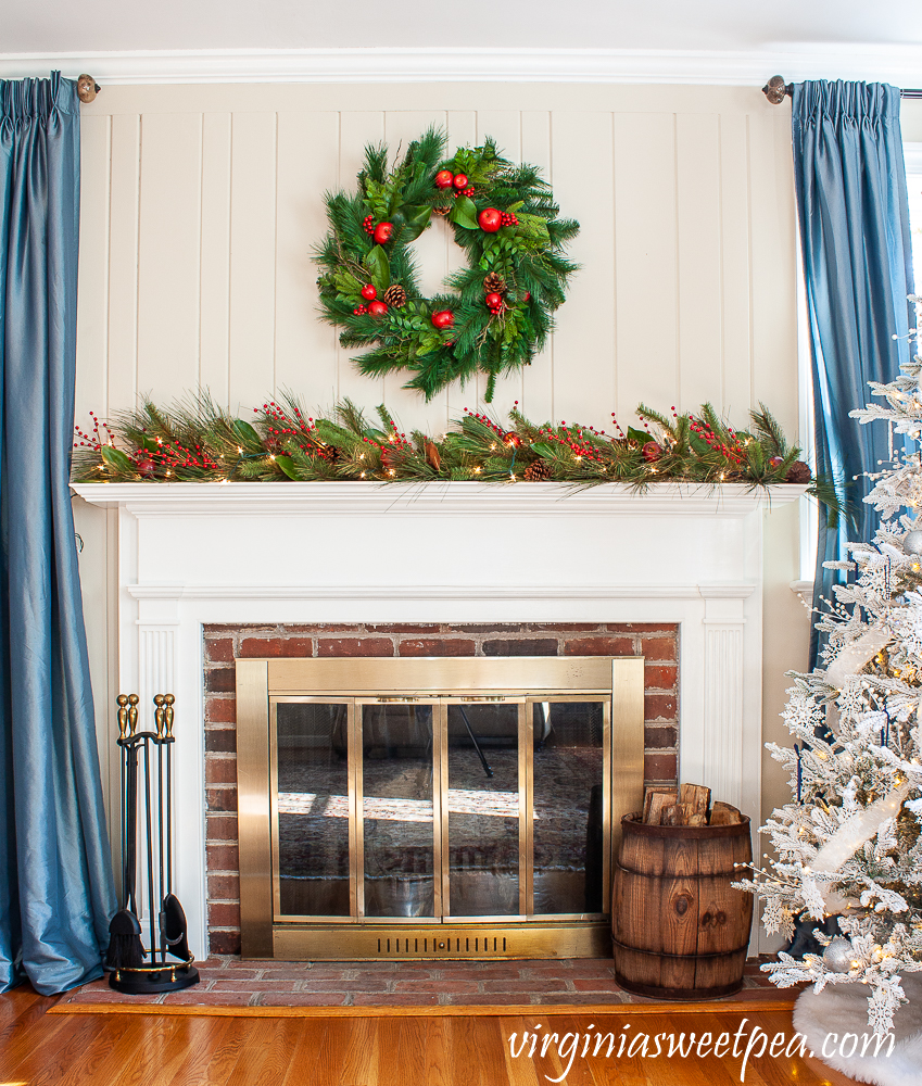 Christmas mantel with Williamsburg wreath and lighted garland on the mantel with red berries, Magnolia, and pine cones.