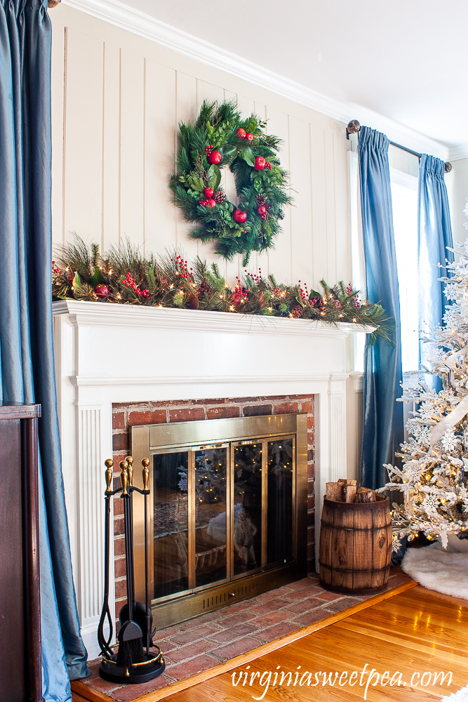 Christmas mantel with Williamsburg wreath and lighted garland on the mantel with red berries, Magnolia, and pine cones.