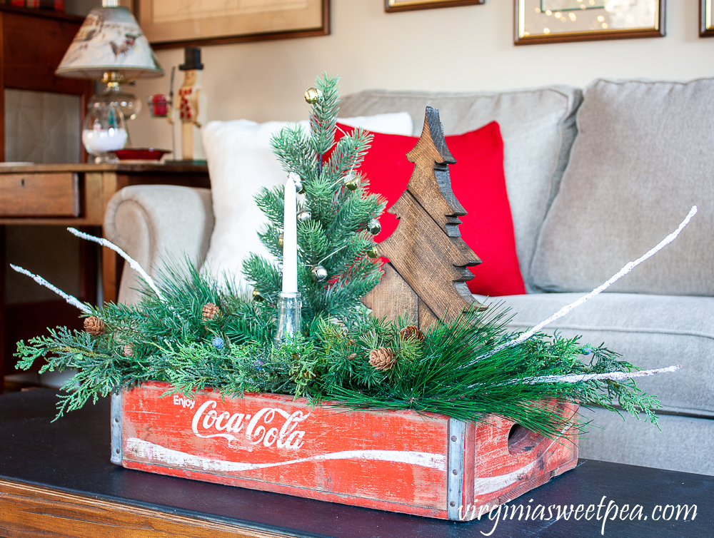 Vintage Coca-Cola crate decorated for Christmas with a wood tree, vintage Coke bottle, and greenery.