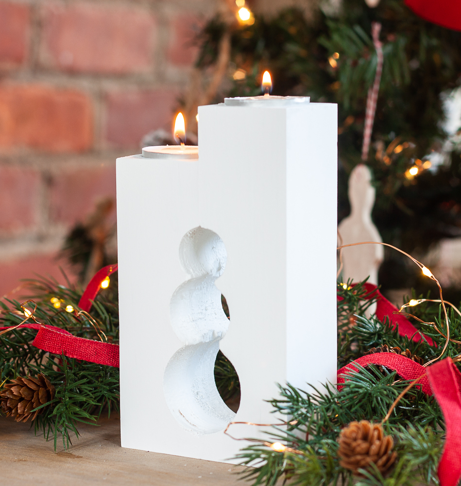 White DIY wooden candle holder with two tea lights and a snowman cut into the wood