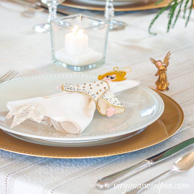 Christmas place setting with vintage silver, a gold charger and white plate, napkin with a vintage 1970s angel napkin holder and a vintage musical angel ornament