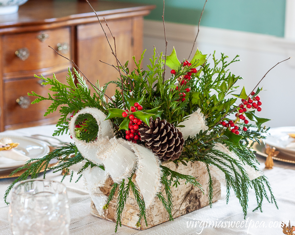 Christmas centerpiece with greenery, Holly, pinecones, twigs, and white ribbon trimmed with gold