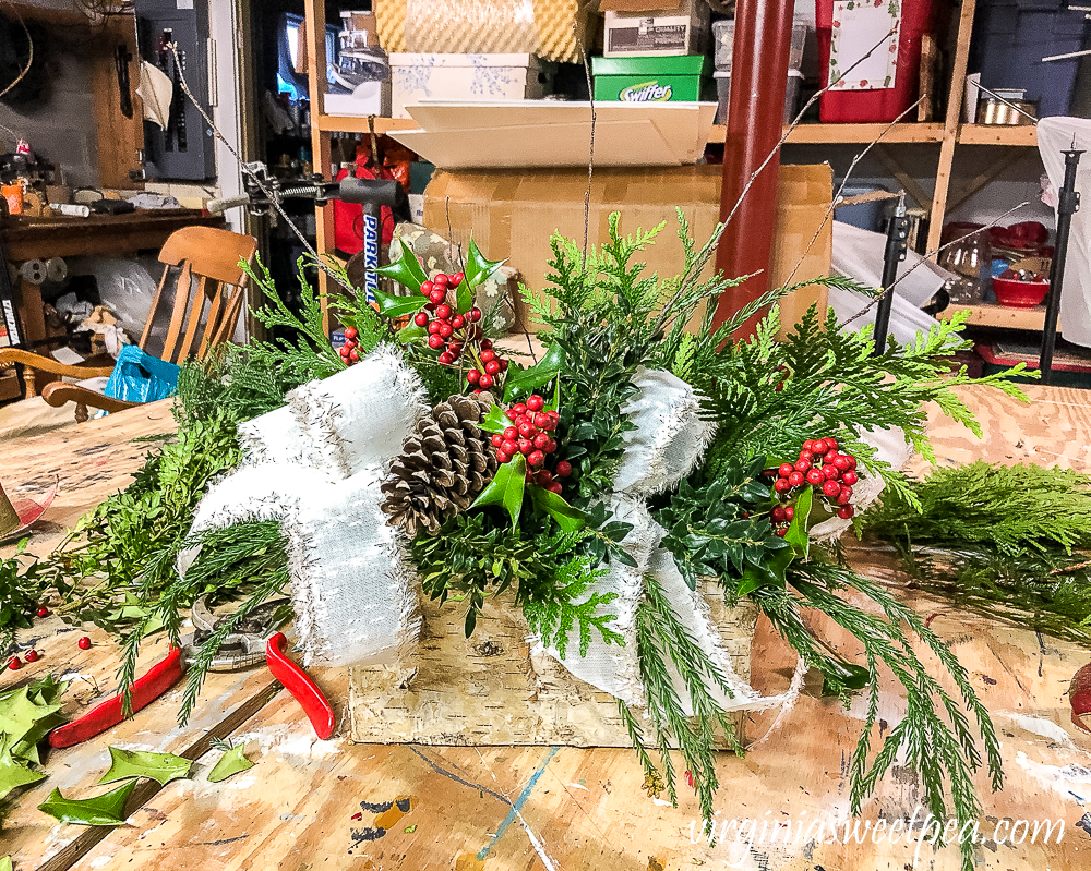 Greenery, pinecones, twigs, and holly in a birch bark floral container
