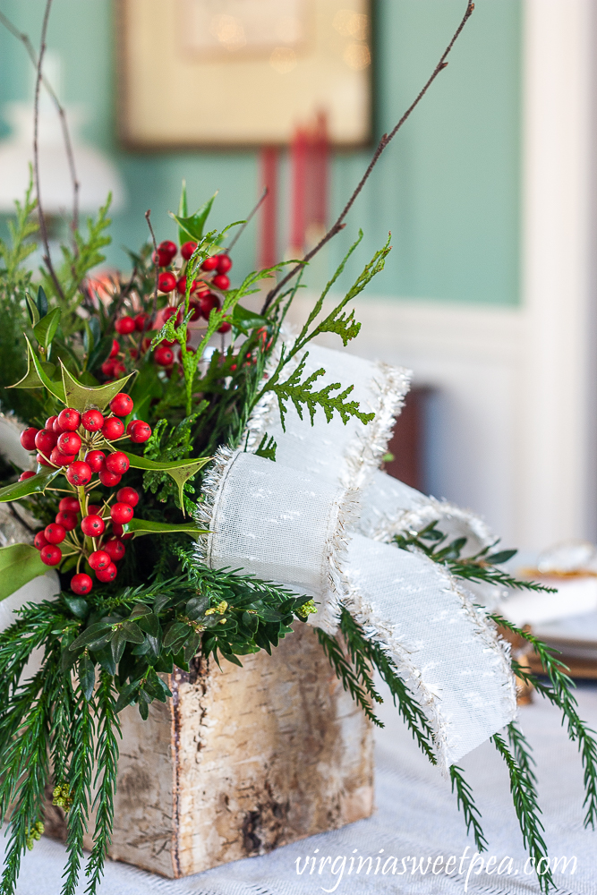 Side view of a Christmas centerpiece in a Birch bark box with greenery, Holly, twigs, and white bows