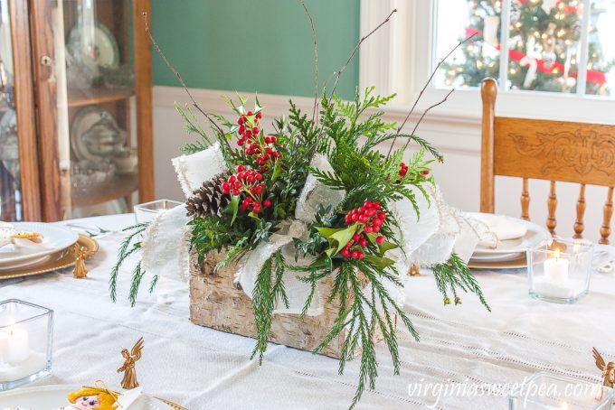 Christmas centerpiece in a Birch bark box with greenery, Holly, pinecones, twigs, and white ribbon trimmed with gold