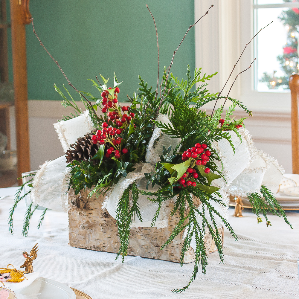 Christmas centerpiece with greenery, Holly, pinecones, twigs, and white ribbon trimmed with gold