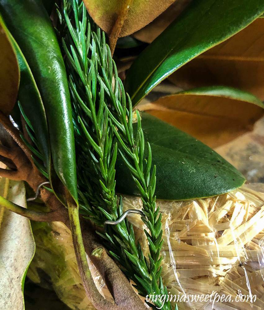 Greenery pinned to a straw wreath form